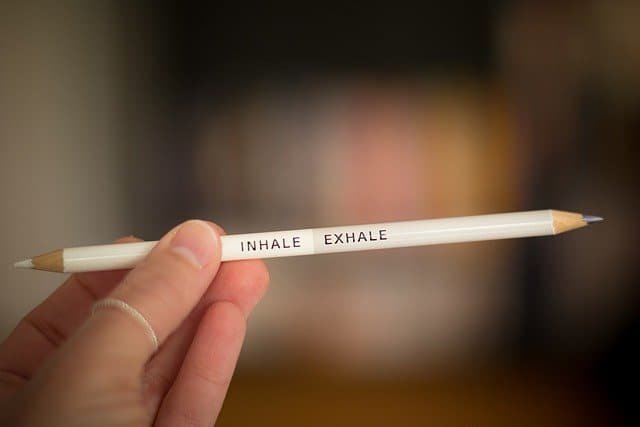 A hand holds a pencil marked "inhale" and "exhale" to represent test anxiety.