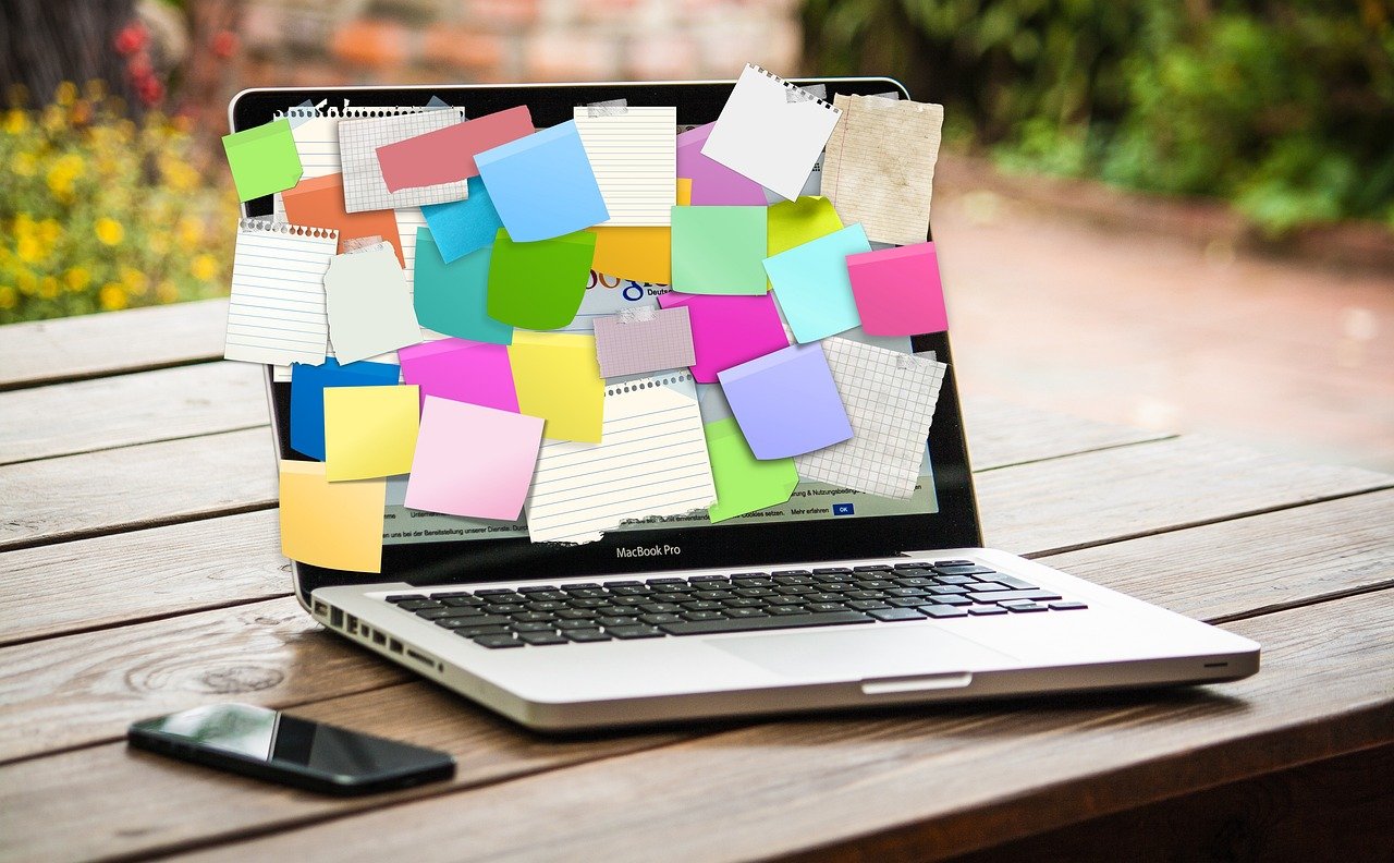 Image of a laptop on a table. The screen is covered with disorganized notes. Digital organization is definitely needed here.