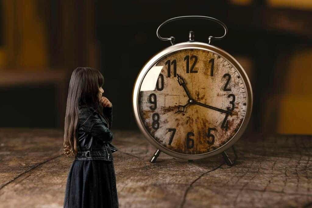 Image of a long haired woman standing in front of a giant clock. She looks like she is pondering the meaning behind the overwhelming time piece. Image is mean to symbolize how time management overwhelms the advise of procrastination cures when time management isn't the problem.
