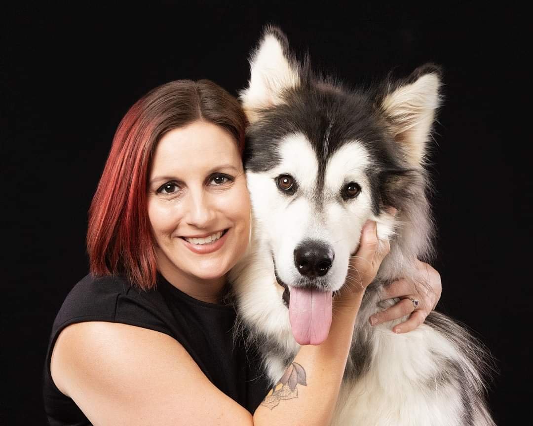 Portrait of instructional designer Ms. Kim McHugh, who found herself in the wrong graduate program, hugging her Malamute. 