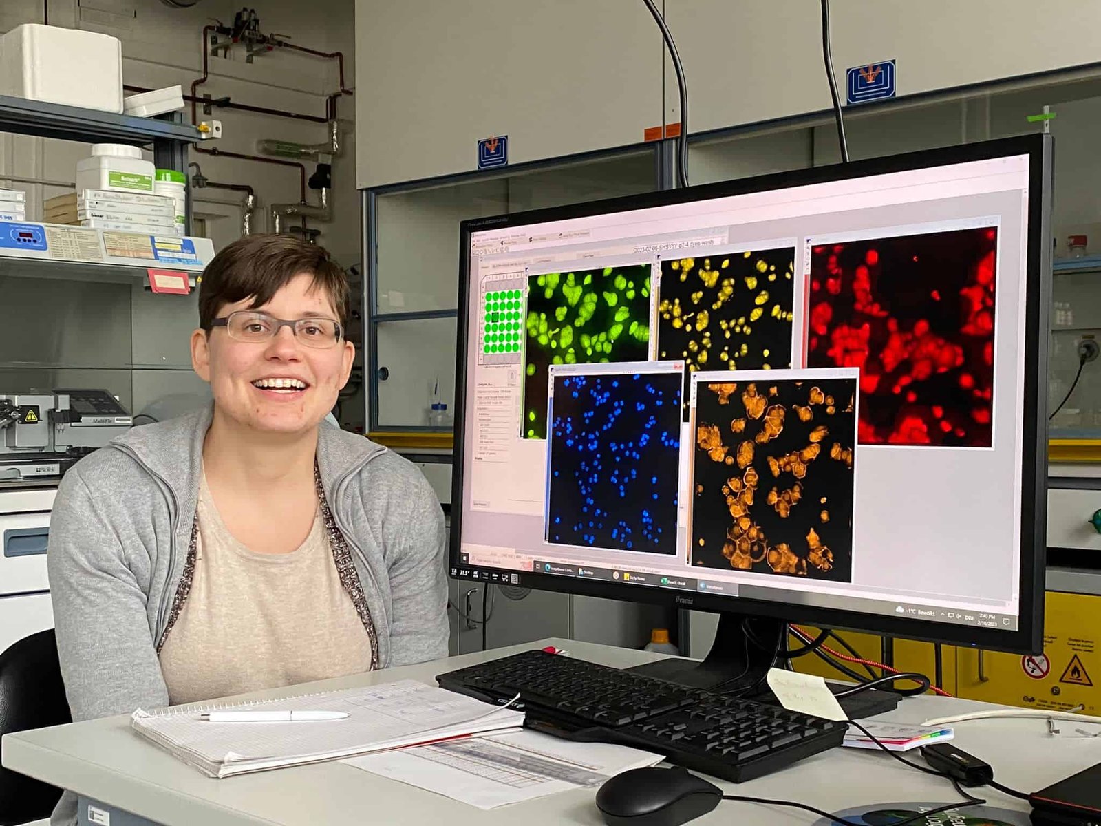 Picture of Dr. Jo Nyffler, sitting to the side of their computer screen which displays several colorful assays.