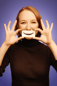 Image of a person holding up a paper smile in front of their mouth, hiding their true expression. The 5th lesson in coaching graduate students.