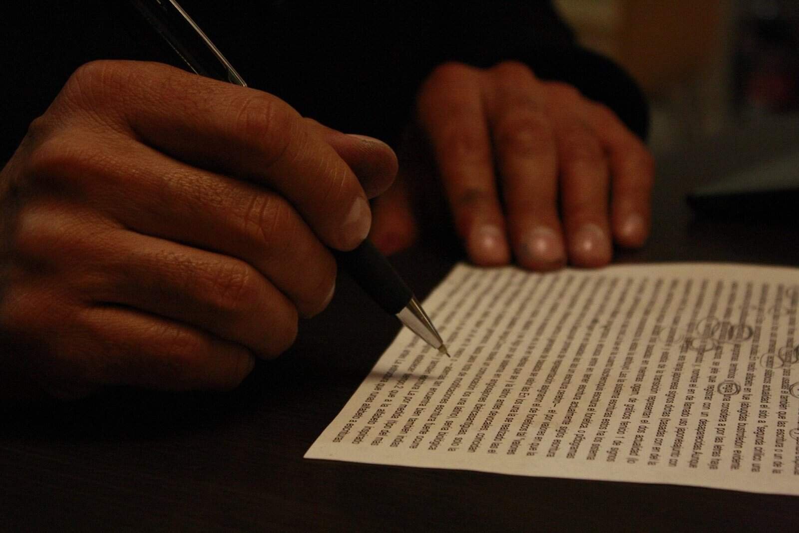 Image shows a set of hands holding a pen over a typed document that is being reviewed. 