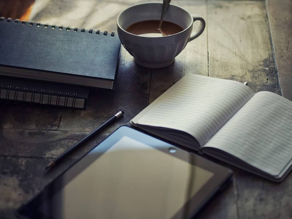Featured image for Personal Statement Review: A photo shows a wooden table with an open notebook, a tablet, a pencil, and a cup of coffee with a text overlay of : Unlock Your Path to Graduate School - Craft the Ultimate Personal Statement.