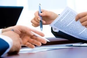 Close up image of a meeting where papers are being discussed. A table has paperwork and hands are shown pointing out corrections.