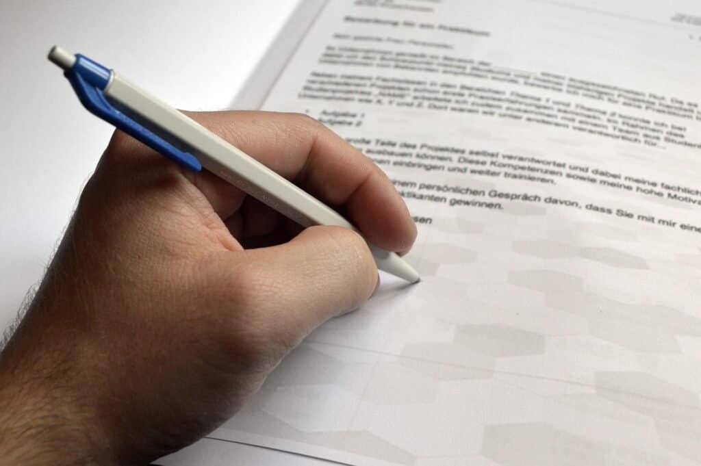 Close-up of a man's hand holding a pen and signing a letter of recommendation.