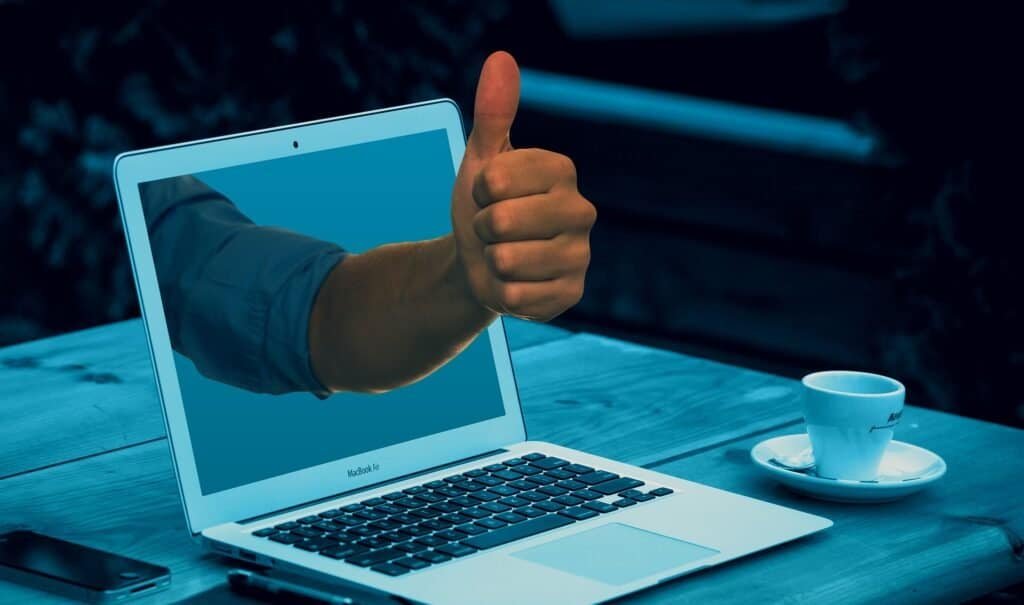 Feature Image for How to Ask for a Letter of Recommendation post depicts a table with a cup of coffee and an open laptop with an arm extending out from the monitor with a big thumbs up.